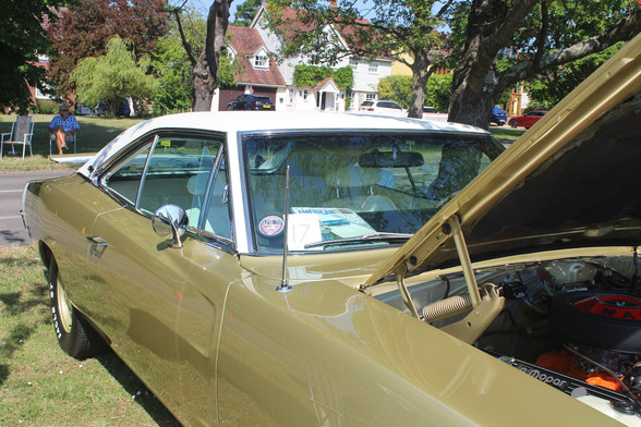 Side view of a Dodge Charger. The car is  gold coloured with a white roof. An American car magazine is visible in the front window.