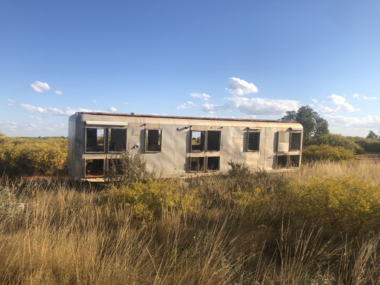 An empty aluminium carriage left in a field of dry grass and acacia bushes