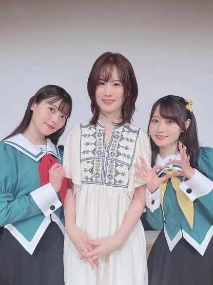 Sumire (as Mitsuki) smiling on the right side of Asami who is smiling. Yui on the left side of Asami, smiling with her hands formed in a heart shape.