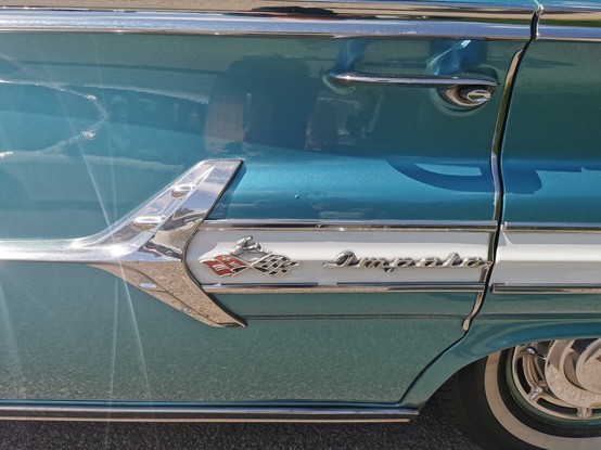The Impala badge on the side of a 1960 Chevrolet Impala the car is Marine Blue with extensive chrome work on the side of the car.