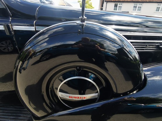 Right hand side of a black 1930's car.
There is a spare wheel carrier built in the wing, this bears the legend Buick. To the right of this the word Special is visible on the side of the the engine housing.
