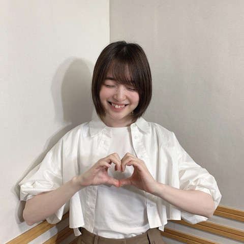 Reina with her eyes closed, smiling while making a heart with her hands.