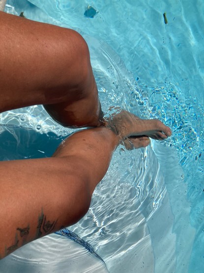 Someone’s bare legs dangling in a swimming pool.