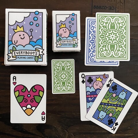 A deck of cards showing a pink, happy, round little smiling creature blowing bubbles. The deck is normal size, there’s also mini cards. Shows the ace of hearts too which is pink and flowery.