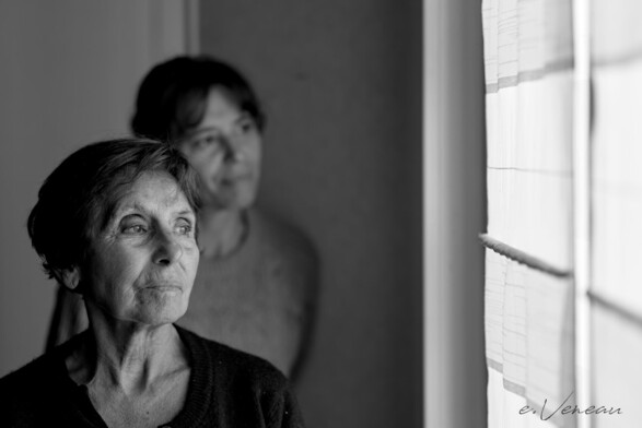 Portraits of a mother and her daughter near a window through which they look.