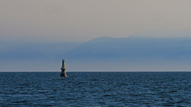 Misty mountains in the far background loom over a rough sea watched over by a lighthouse