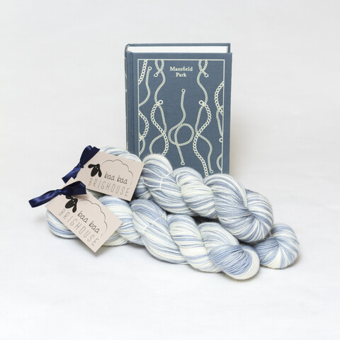 Picture shows three skeins of yarn positioned diagonally in a pyramid. The yarn is grey/blue and white. Behind the yarn is a copy of Jane Austen's Mansfield Park stood on its end. The cover is grey/blue with a repetitive white chain pattern on it.
