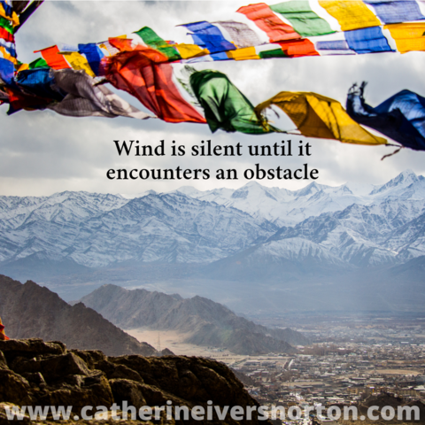 Colorful prayer flags flutter above high mountains. Caption reads, "Wind is silent until it encounters an obstacle."