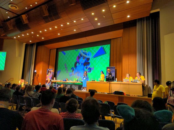 The Galacon main stage, just prior to the start of the charity auction. Some items are visible on a table located on the main stage. The auction benefits the Make A Wish foundation.