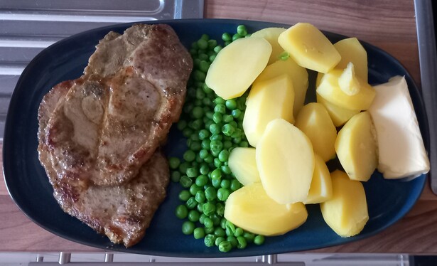 Two pork steaks, peas and boiled potatoes with butter on an oblong blue plate. Dinner.