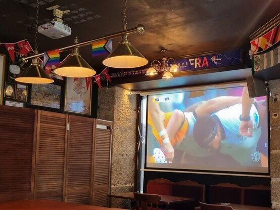 Photo of the interior of a pub. A big screen is showing Australia v Fiji in the Rugby World Cup. Bunting can be seen around the pub, including the inclusive LGBT Pride flag.