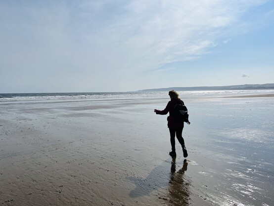 a woman in silhouette walking towards the sea on a beach