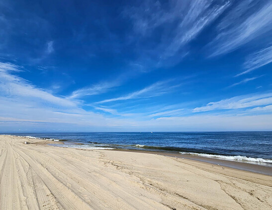 Beach photo of sand, ocean, and deep blue sky with some fair-weather clouds