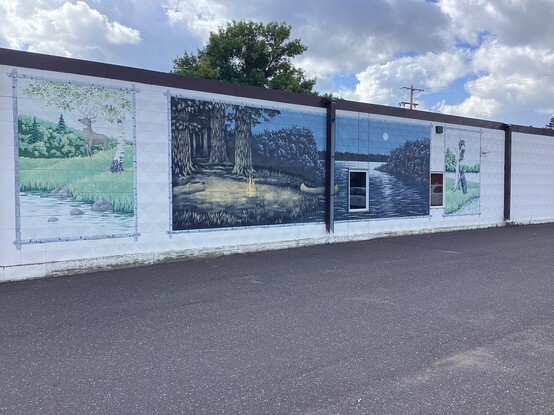 A mural of iconic northern Minnesota scenes, woodlands with deer, night campfires, moonlit rivers on the side of a building in Pine City MN USA