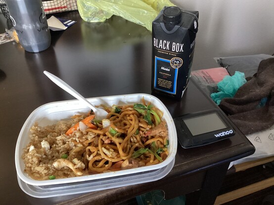 A photo of a container of Lo Mein and a small box of wine on a hotel desk.