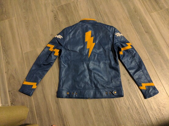 A blue leather or faux leather jacket, with yellow stripes and a thunderbolt added on. The jacket is meant to mimic the Wonderbolts uniforms from My Little Pony. The back of the jacket is visible in this shot.