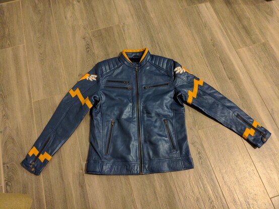 A blue leather or faux leather jacket, with yellow stripes and a thunderbolt added on. The jacket is meant to mimic the Wonderbolts uniforms from My Little Pony. The front of the jacket is shown and features a number of zippered pockets.