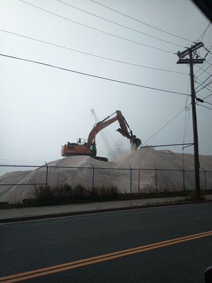 an excavator works to shape a salt pile on the St. John's waterfront against a backdrop of fog