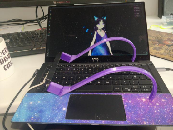 Picture of two curved purple 3D printed plastic arms designed to sit over my shoulders, a block protudes from the front and an Ultraleap StereoIR170 is screwed to them, with the USB cable attached. The whole arrangement is sat on top of a laptop with Lum's VTuber showing on screen
