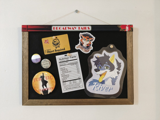 A corkboard with souvenirs: a con badge, pins, a volunteer's emblem, fursona badge and "furry nutrition facts" label, and a "furry trash" sticker. Con lanyard with Fur-Eh! Logo is on top of the frame reads "Broadway Tails".