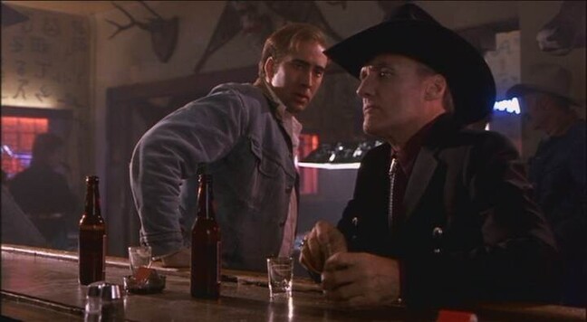 a still from RED ROCK WEST showing a honky tonk, dive bar at nighttime with Nicholas Cage and Dennis Hopper sharing a beer