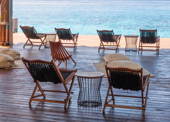 Low slug seats, tables and pillows on a plank floor in front of the sea.