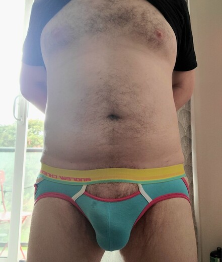 man posing infront of his balcony, with his chest and belly exposed showing only his jock strap. His bluge clearly visible also some precum can be seen leaking
