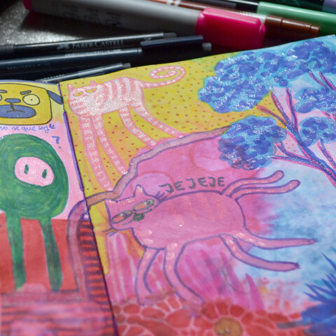 A picture of a notebook, showing some color doodles of cats, dogs a tree and some green round creature.