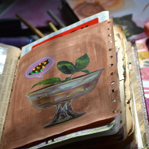 A picture of a notebook showing a collage, there's a cup, a plant and a sticker of a turtle.