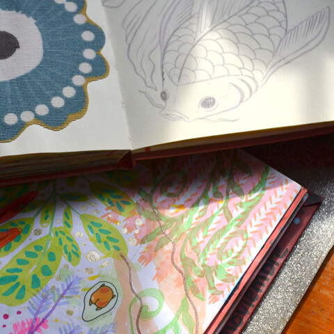 A picture of two notebooks, one showing a sketch of a koi fish, the other one showing some color doodles of plants.