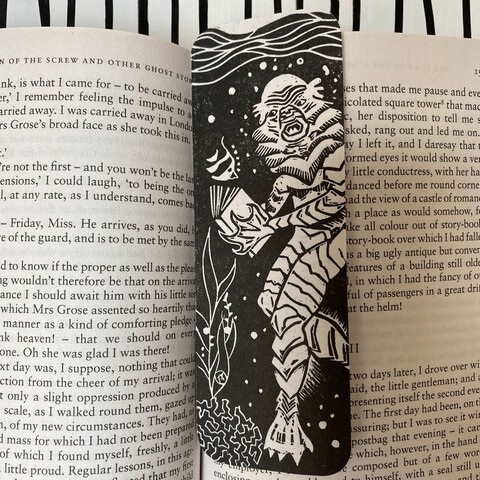 A linocut bookmark featuring the classic movie monster Gillman reading horror stories to a little fish friend.