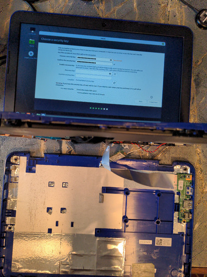 A small Dell laptop lying on the back of the screen with the bottom of the laptop removed. Bits of circuit board and wiring are visible. The laptop screen is on, and the laptop shows an installation of Linux Mint in progress.