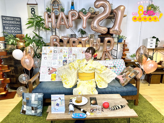 Sayuri wearing a kimono sitting on a bench with balloons indicating her 21st birthday with stuff spread out on the table.