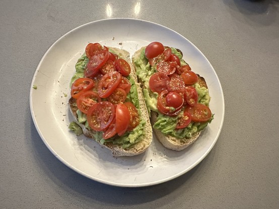 Plate with two pieces of home made sourdough bread covered in mashed avocado and sliced up cherry tomatoes.