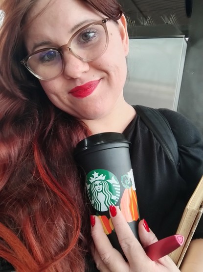 A selfie of me standing in the wind and holding a pumpkin themed reusable to go cup, my notebook and my pen.
