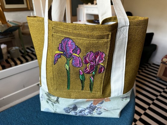 Fabric grocery bag/tote.

Mustard yellow, with cream coloured straps, a pale green and flowery bottom. Front pocket has two embroidered pink and purple lilies.