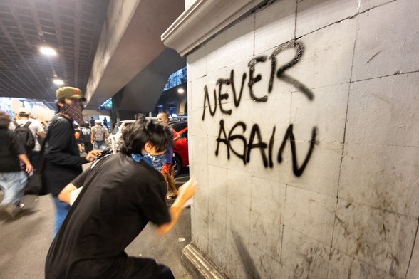 A person writing graffiti of “Never Again” on the wall