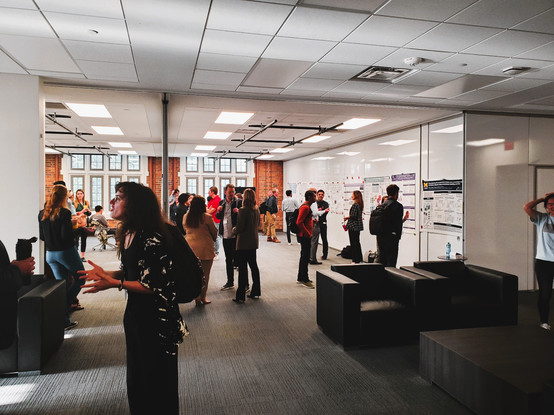 Photo of a poster session at a scientific conference--it's a view toward white walls with individuals standing by their posters and having discussions with other attendees.