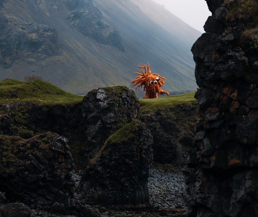 Photo of a rocky coastline where I’ve used generative AI tools to insert an orange monster at the top of a grassy cliff. 

This orange monster has three googly eyes, one arm-like appendage, and lots of very thick dreadlock-like extensions, coming out of the top of its head from various directions.