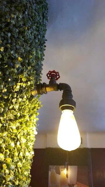 Muro forrado de follaje artificial con una lámpara incandescente montada en un grifo, de forma que el foco encendido parece una gota .