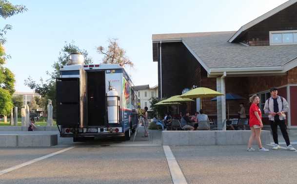 View of a scene outside the Silo. Instead of being parked under the outdoor shelter UC Davis reserves for approved food trucks, this food truck drove down along the side of the Silo Market, blocking the path not just with the food truck, but with an A-board sign menu. It's not convenient for pedestrians who aren't planning on being customers, but it makes it very difficult for mobility aid users and/or folks with vision disabilities to get through an area where cars are not supposed to be parked.