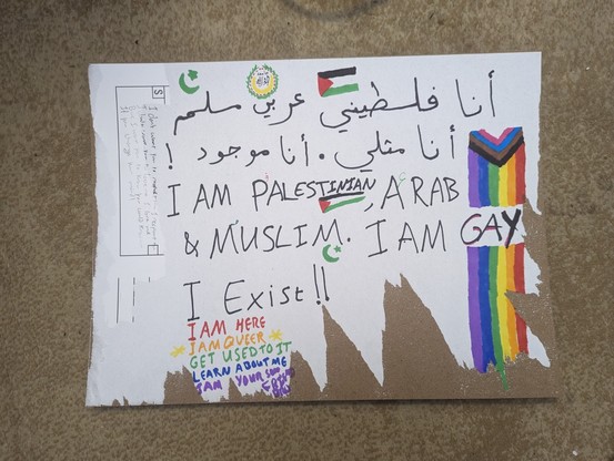 A protest sign that says:
أنا فلسطيني عربي مسلم
أنا مثلي . انا موجود!
I am Palestinian, Arab and Muslim. I am gay. I exist.

A progressive rainbow flag goes through the word gay. A Palestinian flag is next to the word Palestinian. The symbol of the Arab League is above the word Arab. A crescent and a five-pointed star is above the word Muslim.

On the margin are the words:
I am here
* I am queer *
Get used to it
Learn about me
I am your son, friend, bro.

The lyrics to "change your mind" by Rebecca Sugar are on another margin.