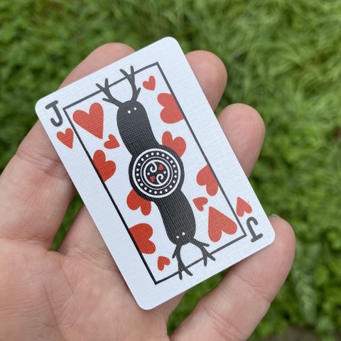 A tiny playing card held on my outstretched fingers. It is the jack of hearts. The jack is a simple black silhouetted creature with tiny white eyes and antlers. Hearts are spread out behind it.
