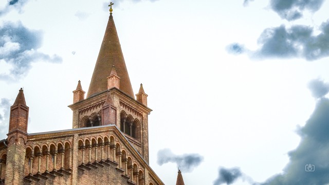 Tower and roofline of beige brick neo-Romanesque church against a grey cloudy sky