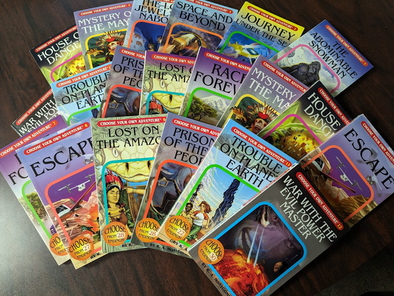 About 20 Choose Your Own Adventure books spread out on a table.