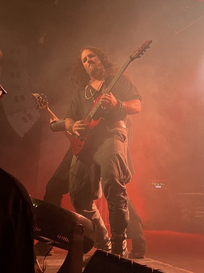 Two guitarists stand back to back, backlit by red lights on a smoky stage.