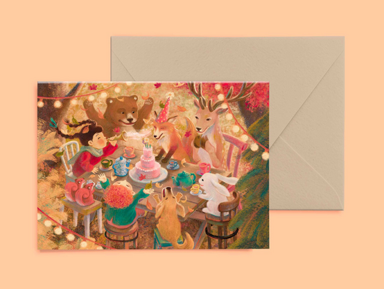 Product photo of a greeting card and an envelope. The illustration on the card features a woodland birthday party with kids and animals around the table.