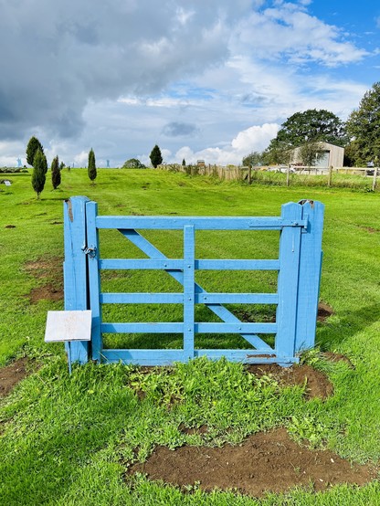a blue gate not attached to a fence in the middle of a field. a small sign next to the gate reads: please shut the gate!