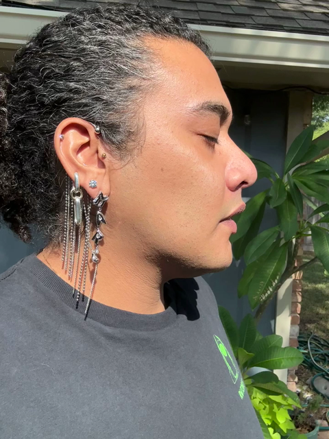 Queer poc individual standing in sunlight showing off silver earrings