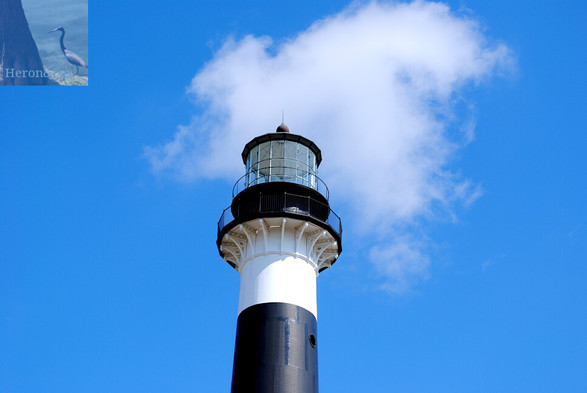 An outdoor photograph look up at the top of a lighthouse tower and its light. The light section and platform are pained black, with a white stripe below it, and another black stripe below it.
